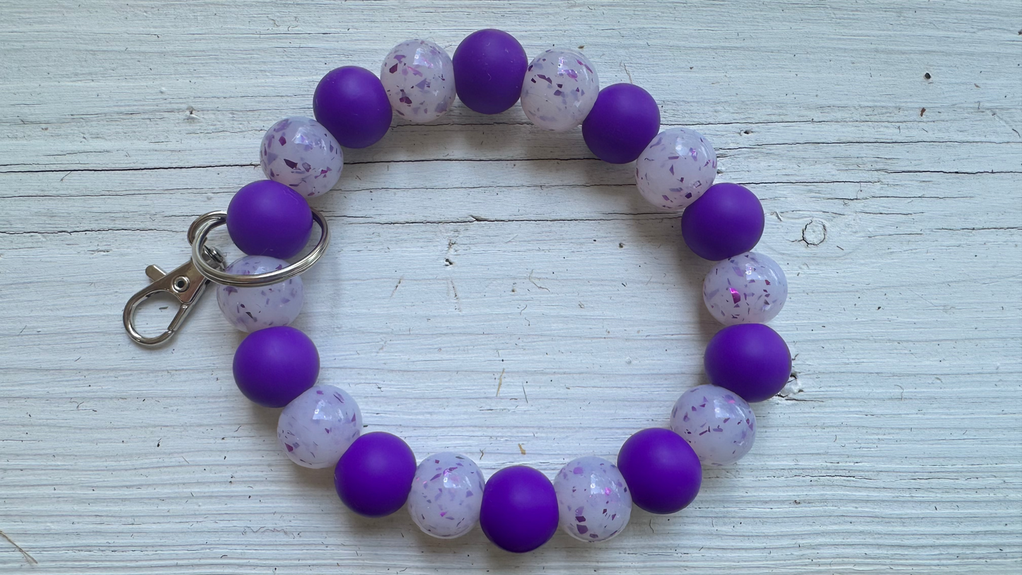 Beaded keychain with purple and speckled beads on a wooden surface