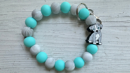 Bracelet with turquoise and gray beads and a dog charm on a wooden surface