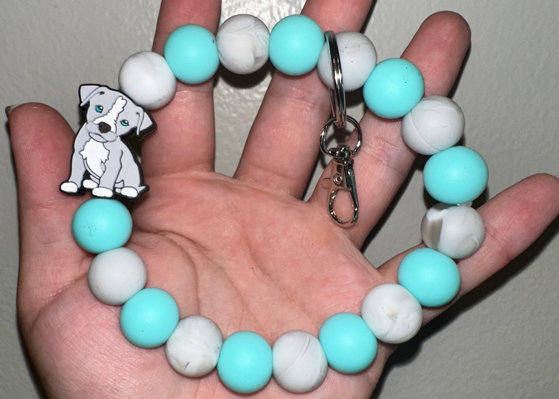 Hand holding a keychain with turquoise and white beads and a dog charm.