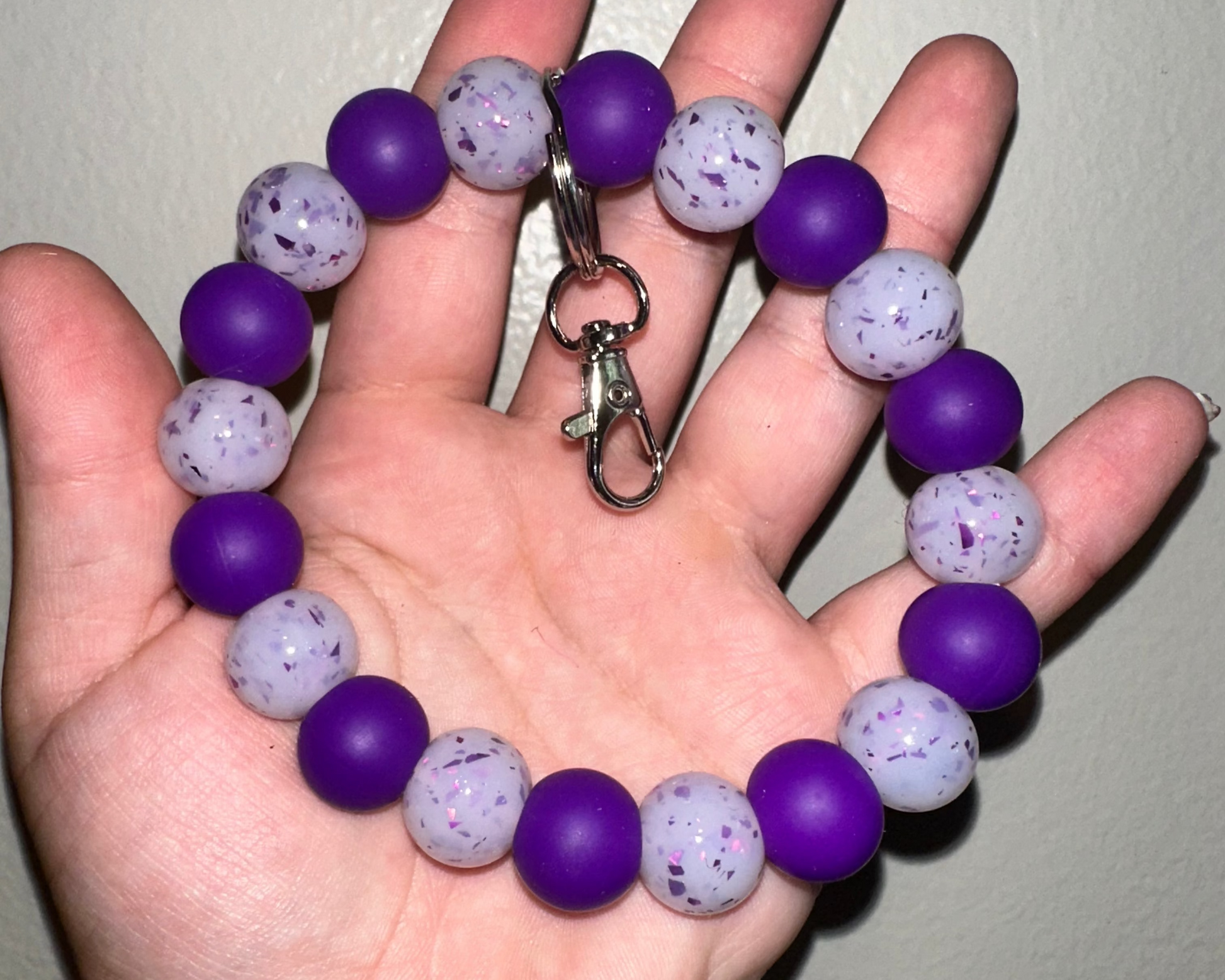 Hand holding a purple and gray beaded keychain against a plain background