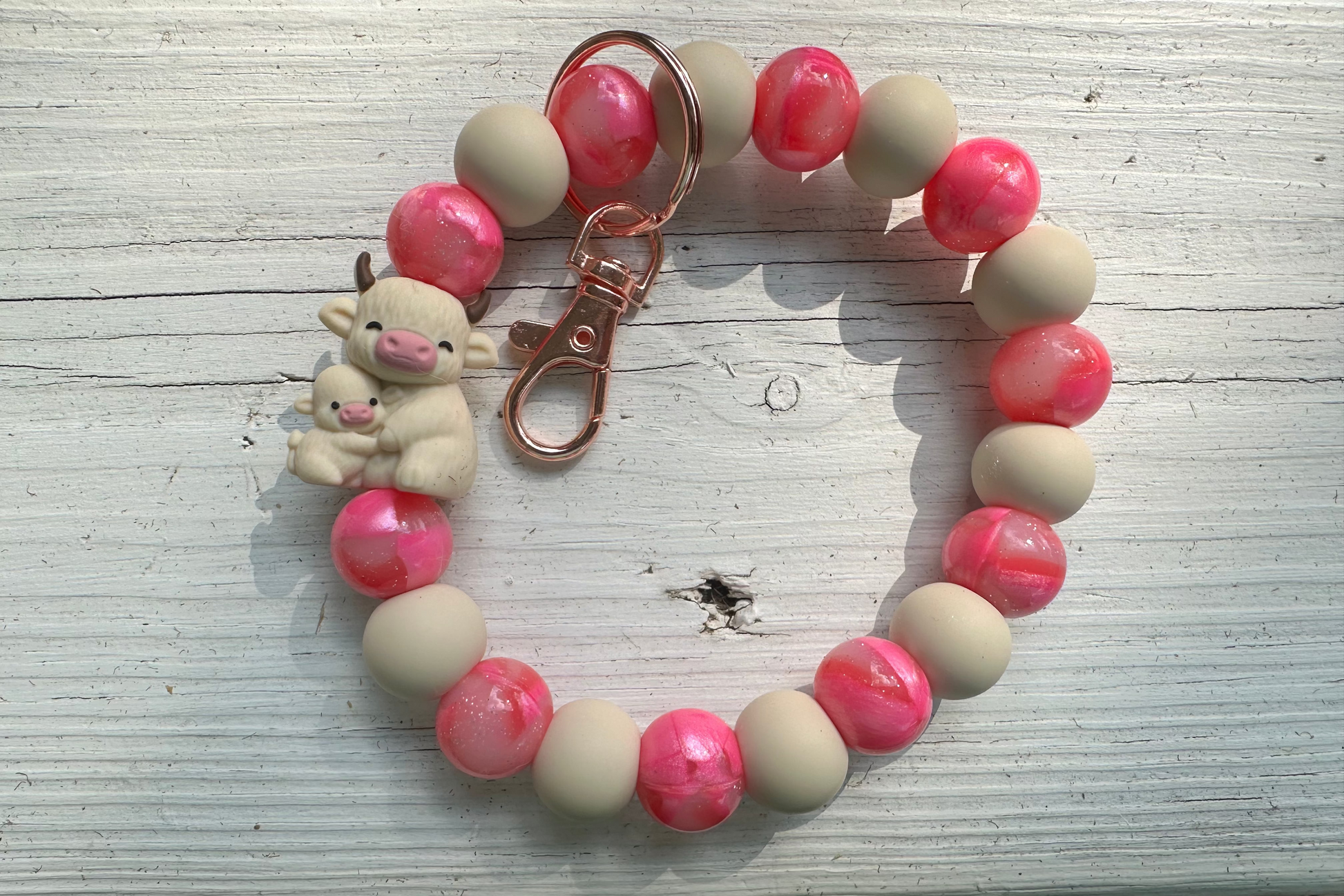 Bracelet with pink and beige beads and a small bear charm on a wooden surface