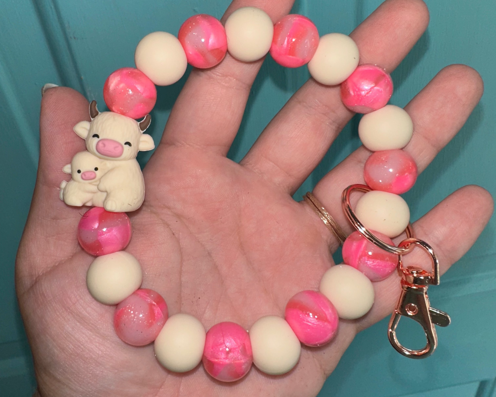 Hand holding a bracelet with pink and white beads and a keychain against a teal background