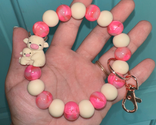 Hand holding a bracelet with pink and white beads and a keychain against a teal background