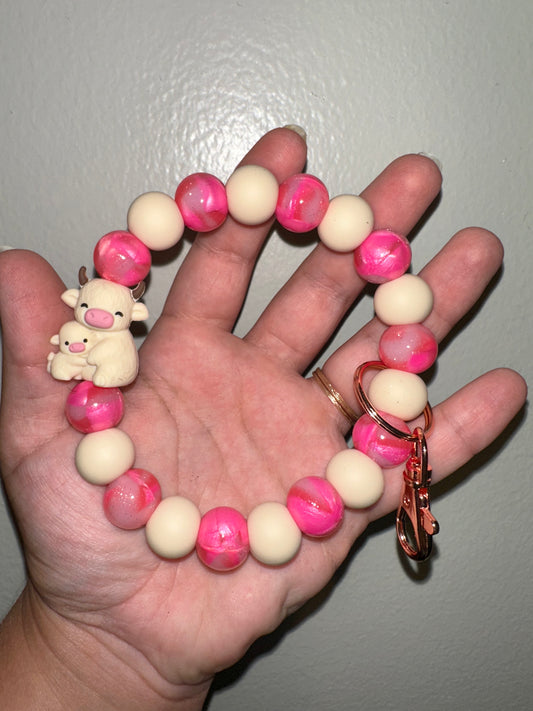 Hand holding a bracelet with pink and white beads and a keychain on a plain background